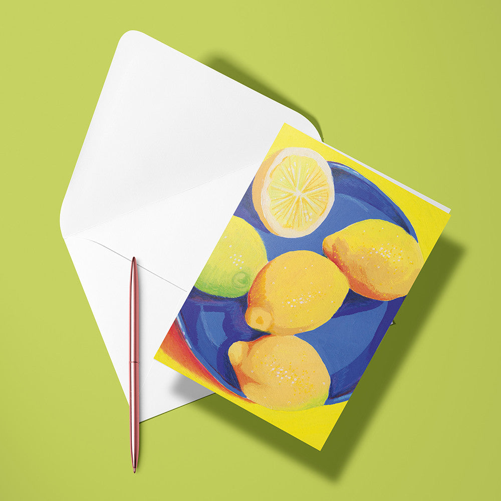Carte pliée Citrons posée avec un stylo doré et son enveloppe sur un fond vert anis