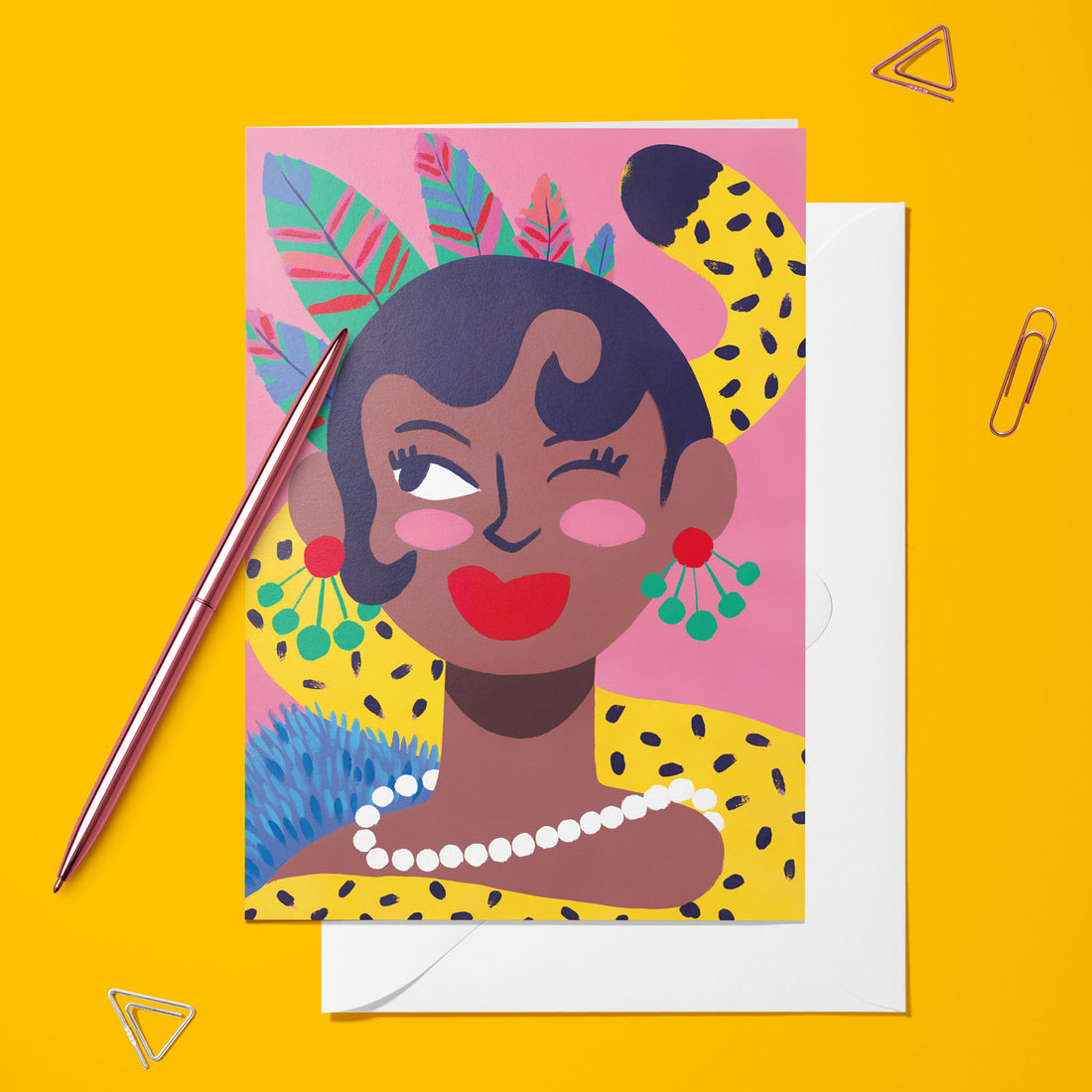 Carte pliée Joséphine posée avec un stylo doré et son enveloppe, portrait au collier de perles