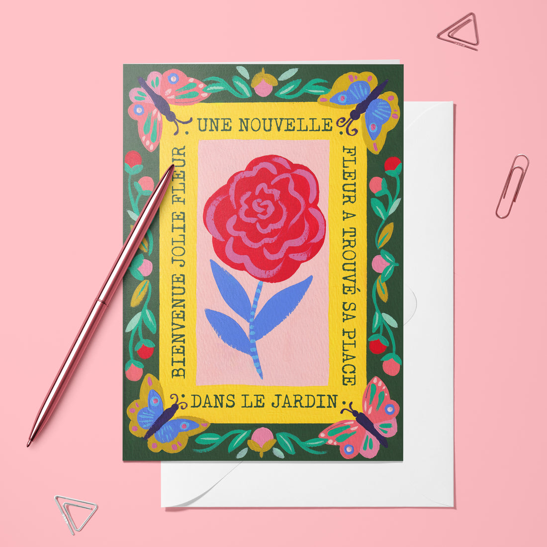 Carte pliée Une nouvelle fleur dans le jardin posée avec un stylo doré et son enveloppe, rose dans un cadre fleuri