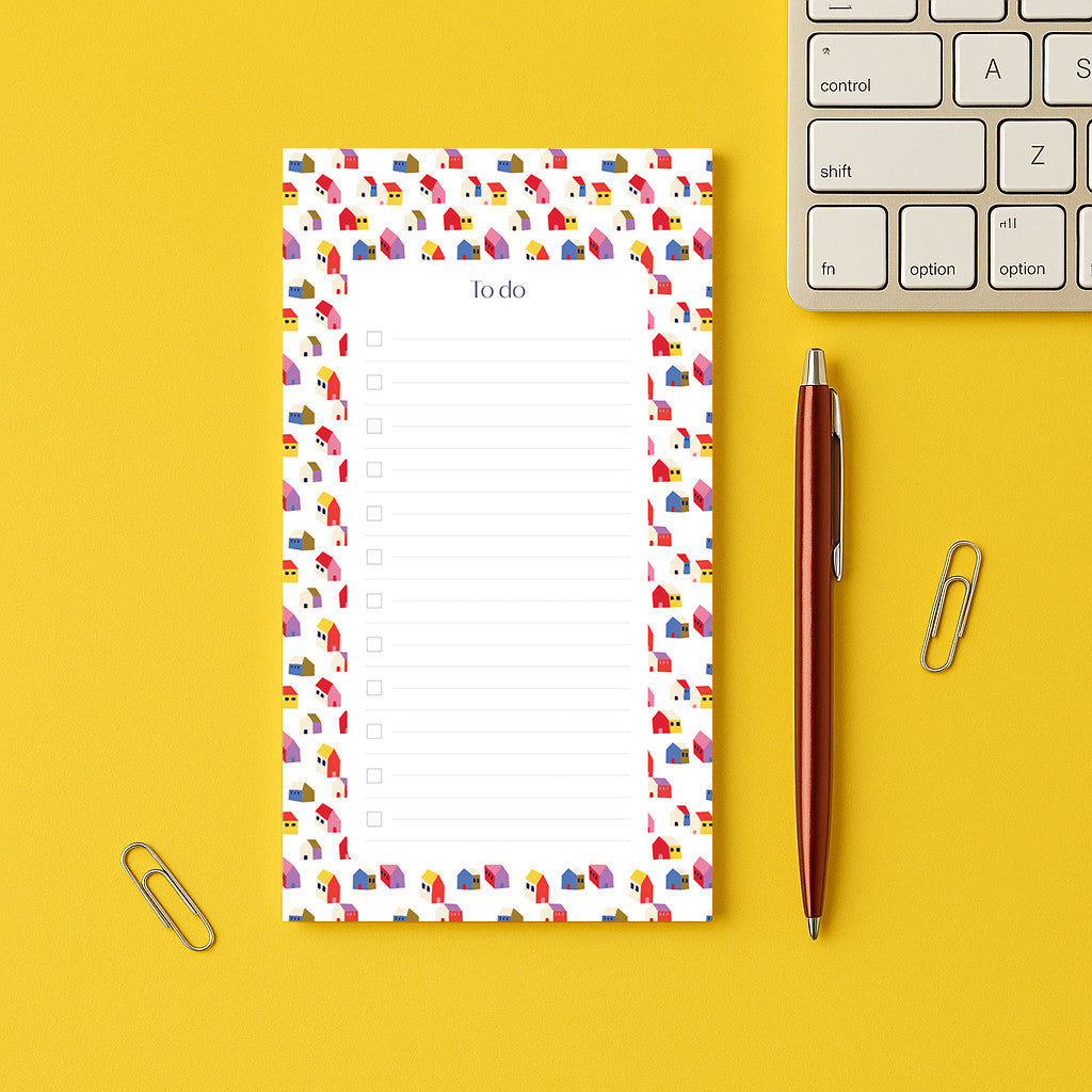 Bloc-notes Maisonnettes posé sur un bureau jaune, liste à cocher encadrée de petites maisons colorées
