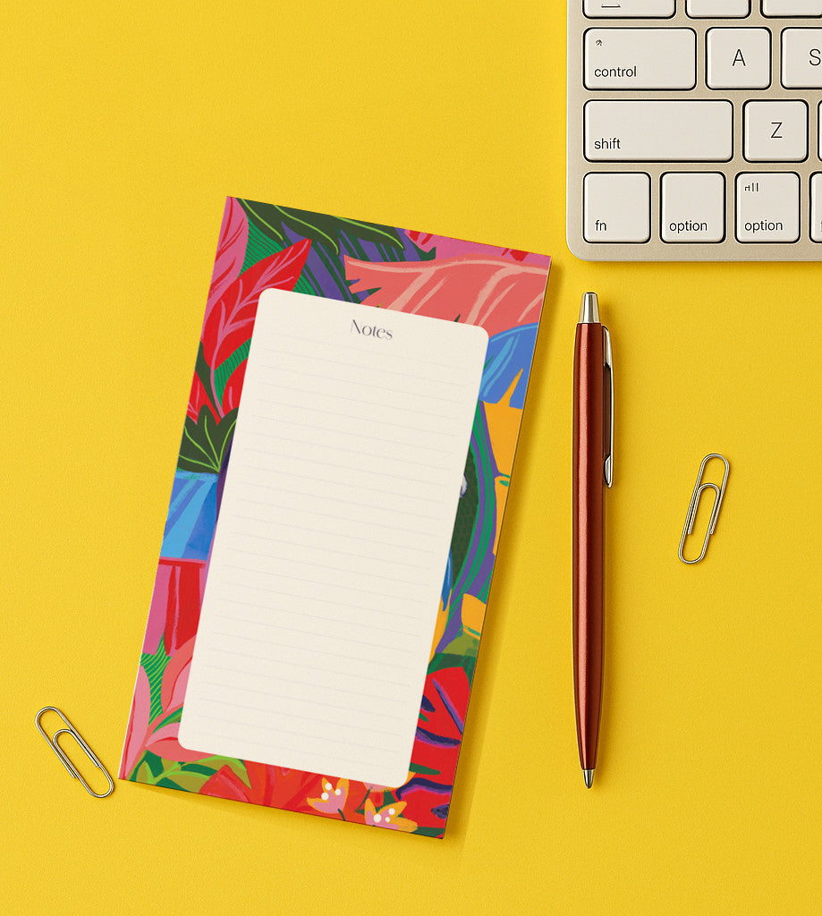 Bloc-notes Feuilles exotiques posé sur un bureau jaune, bordure de feuillages tropicaux, près d'un clavier