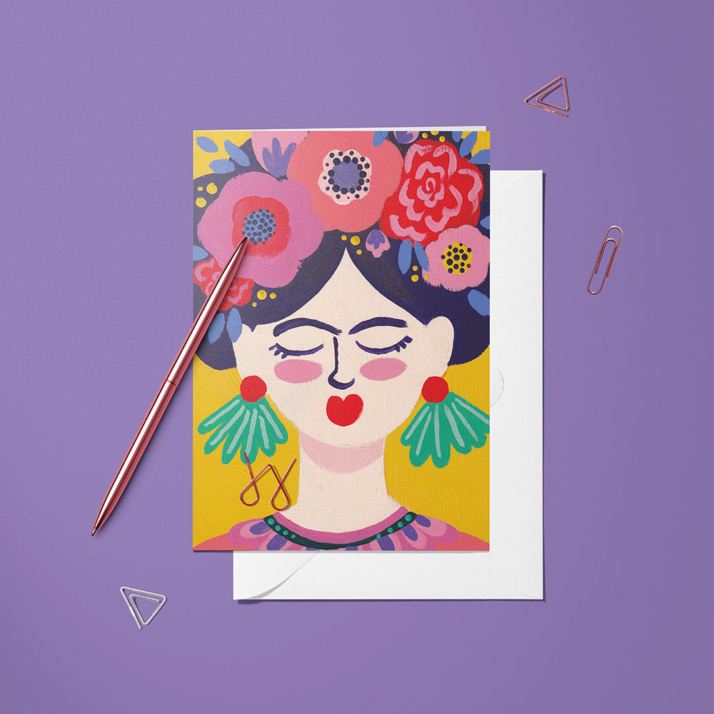 Carte pliée Frida posée avec un stylo doré et son enveloppe, portrait de femme couronnée de fleurs