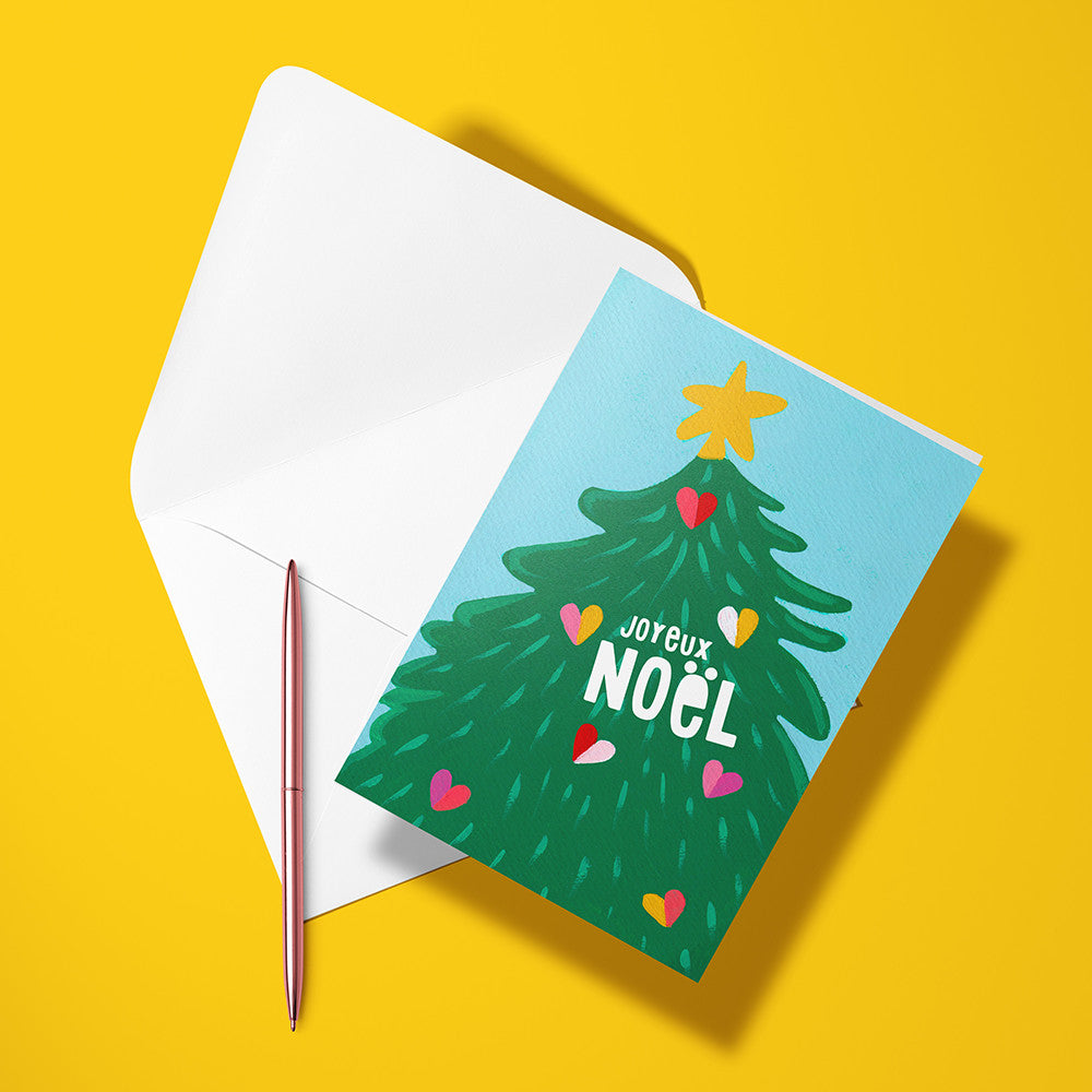 Carte pliée Sapin aux cœurs posée avec un stylo doré et son enveloppe, sapin vert décoré de petits cœurs