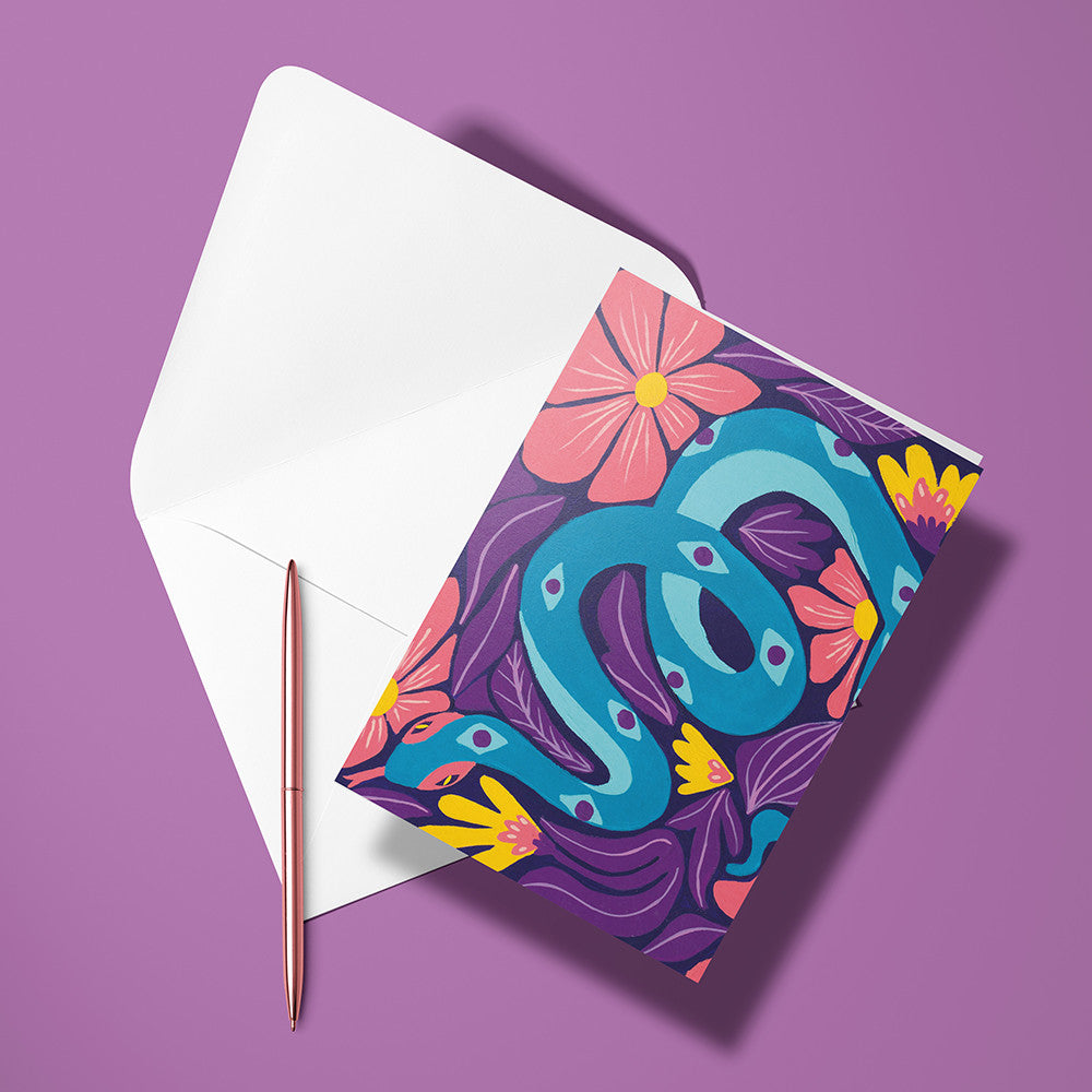 Carte pliée Serpent posée devant son enveloppe ouverte, serpent turquoise parmi les fleurs sur fond violet