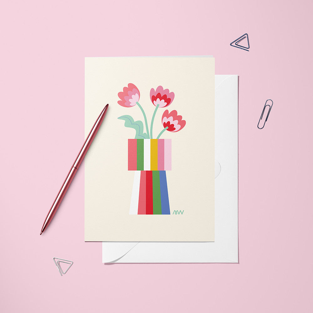Carte pliée Vase Bandes de Couleur posée avec un stylo doré et son enveloppe sur un fond rose