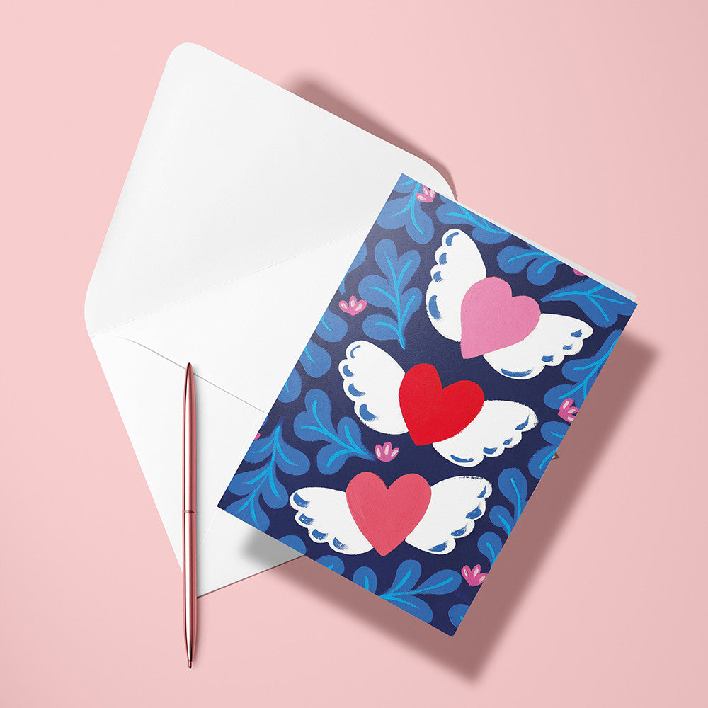 Carte Saint Valentin et son enveloppe posées avec un stylo doré sur fond rose
