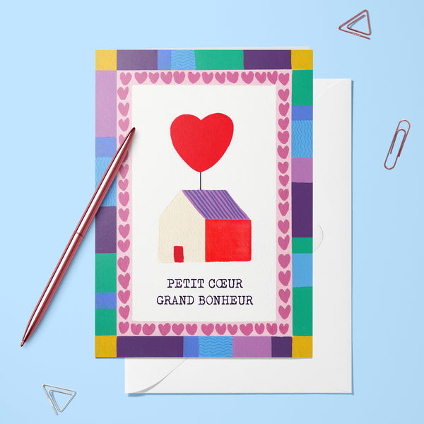 Carte pliée Petit cœur, grand bonheur posée avec un stylo doré et son enveloppe, maisonnette et ballon en forme de cœur
