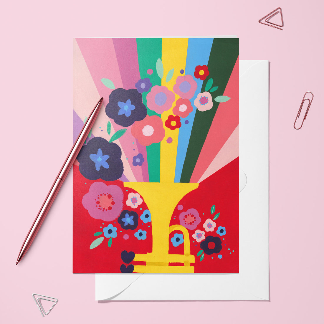 Carte pliée Trompette fleurie posée avec un stylo doré et son enveloppe, trompette dorée d'où jaillissent des fleurs