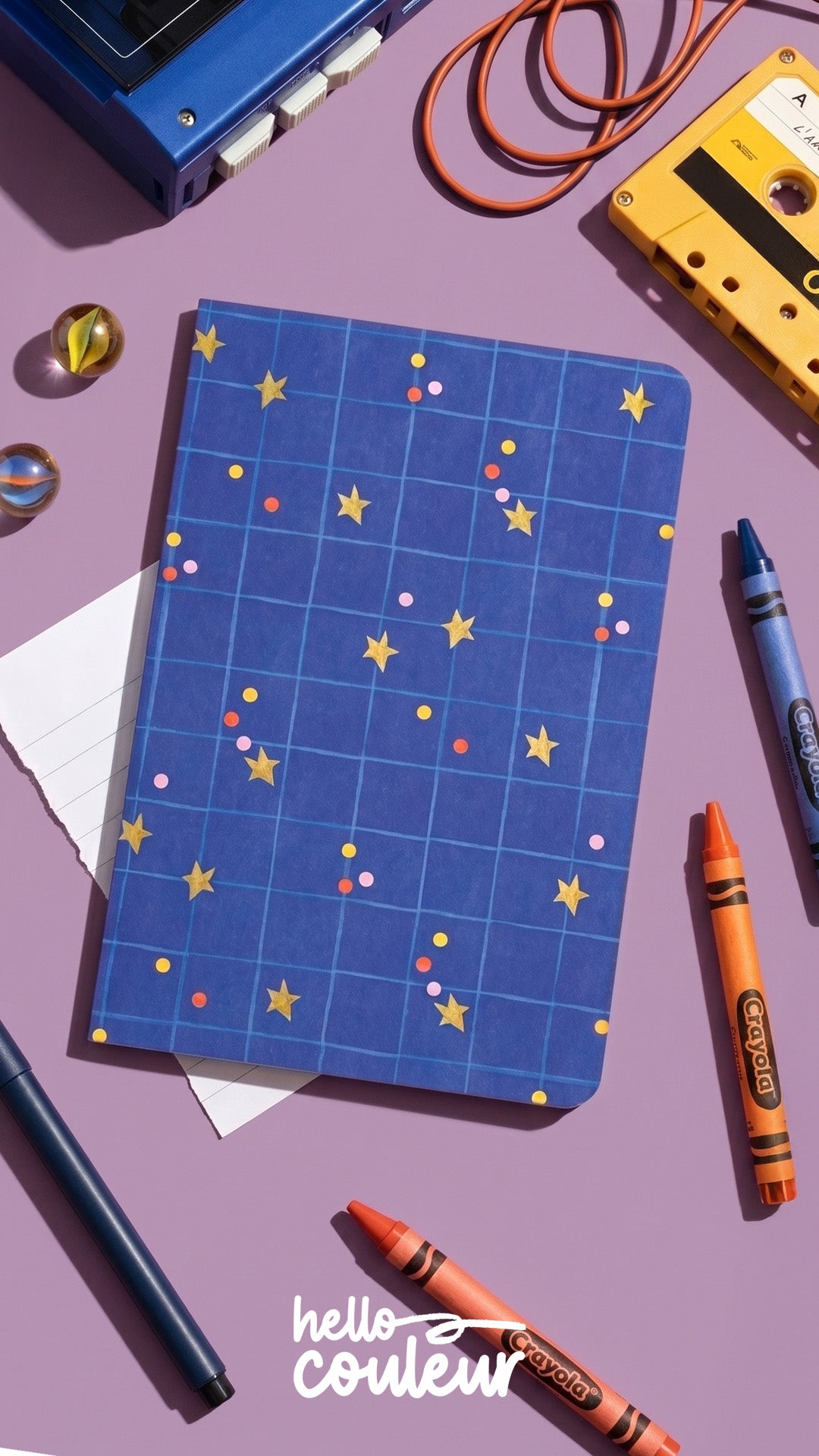 Carnet A5 Stella posé sur un bureau violet, parmi des craies de couleur et une cassette audio