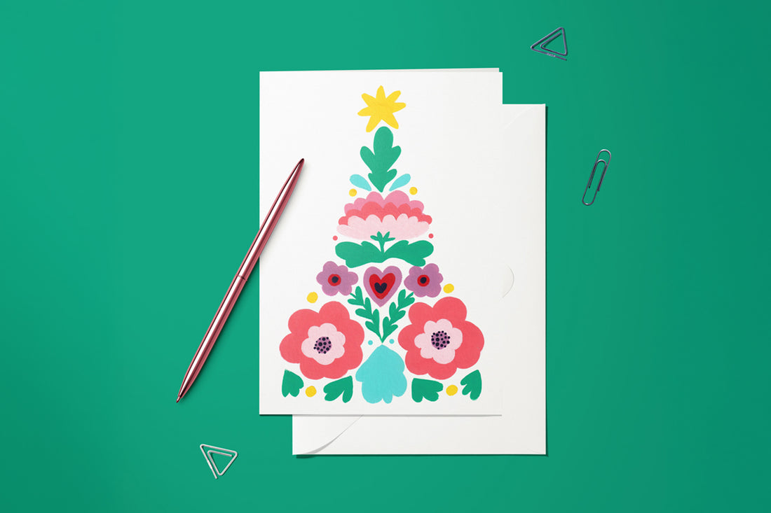 Carte Sapin Scandinave du pack thème Noël, posée avec un stylo doré et son enveloppe sur fond vert