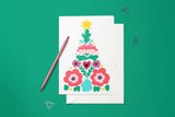 Carte Sapin Scandinave du pack thème Noël, posée avec un stylo doré et son enveloppe sur fond vert