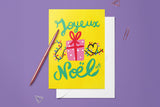 Carte Noël Paquet cadeaux du pack thème Noël, posée avec un stylo doré et son enveloppe sur fond violet