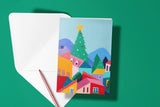 Carte Village de Noël fleuri du pack thème Noël, posée avec un stylo doré et son enveloppe sur fond vert