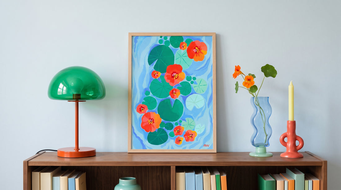 Tirage d'art Nénuphares encadré en bois clair, posé sur une bibliothèque basse entre une lampe verte et un vase de capucines