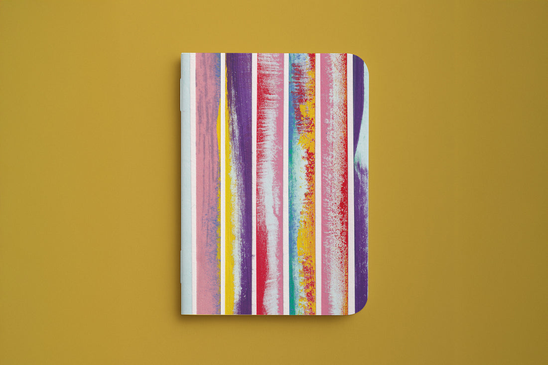 Carnet rayé du trio papeterie coloré, couverture aux rayures verticales peintes, sur fond moutarde