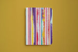 Carnet rayé du trio papeterie coloré, couverture aux rayures verticales peintes, sur fond moutarde