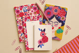 Grand pack Frida déballé à plat : carnets fleuris, carte illustrée, bloc-notes et crayons de couleur