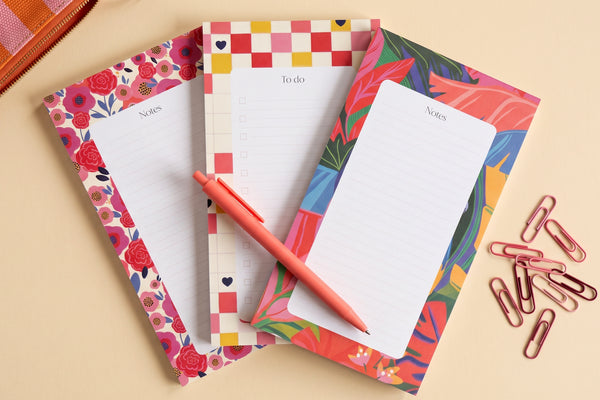 Pack 3 blocs déballé à plat : trois blocs-notes à bordures illustrées, un stylo et des trombones