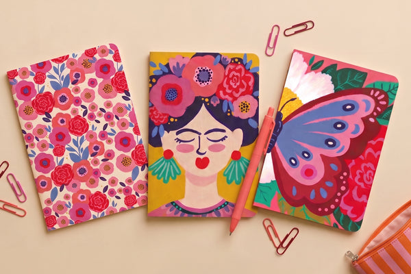 Pack 3 carnets A5 au choix présenté à plat : carnets floral, Frida et papillon avec crayons et trombones