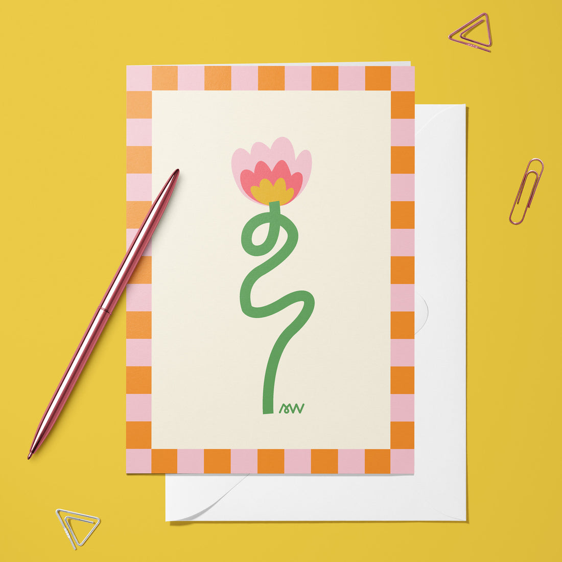 Carte pliée Fleur du bonheur posée avec un stylo doré et son enveloppe sur un fond jaune