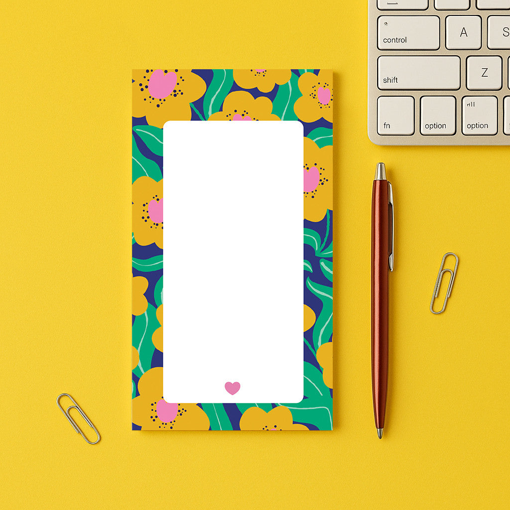 Bloc-notes Pensées posé sur un bureau jaune, bordure de fleurs jaunes sur feuillage vert et petit cœur rose