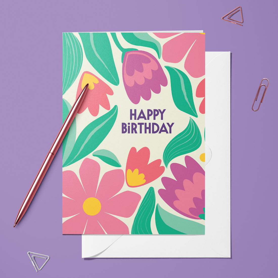 Carte pliée Happy Birthday rétro posée avec un stylo doré et son enveloppe, message entouré de fleurs roses