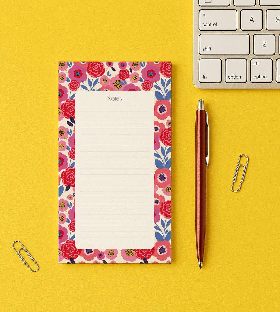 Bloc-notes Festival de fleurs posé sur un bureau jaune, bordure de fleurs roses et rouges, près d'un stylo