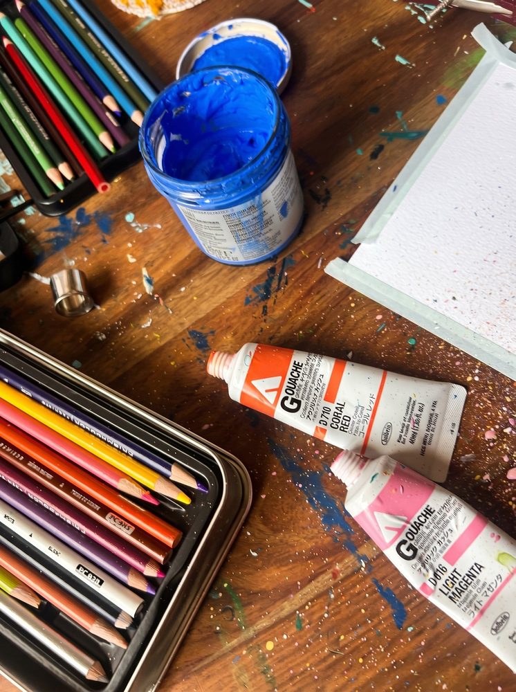 Plan de travail avec gouaches, crayons et illustrations en cours